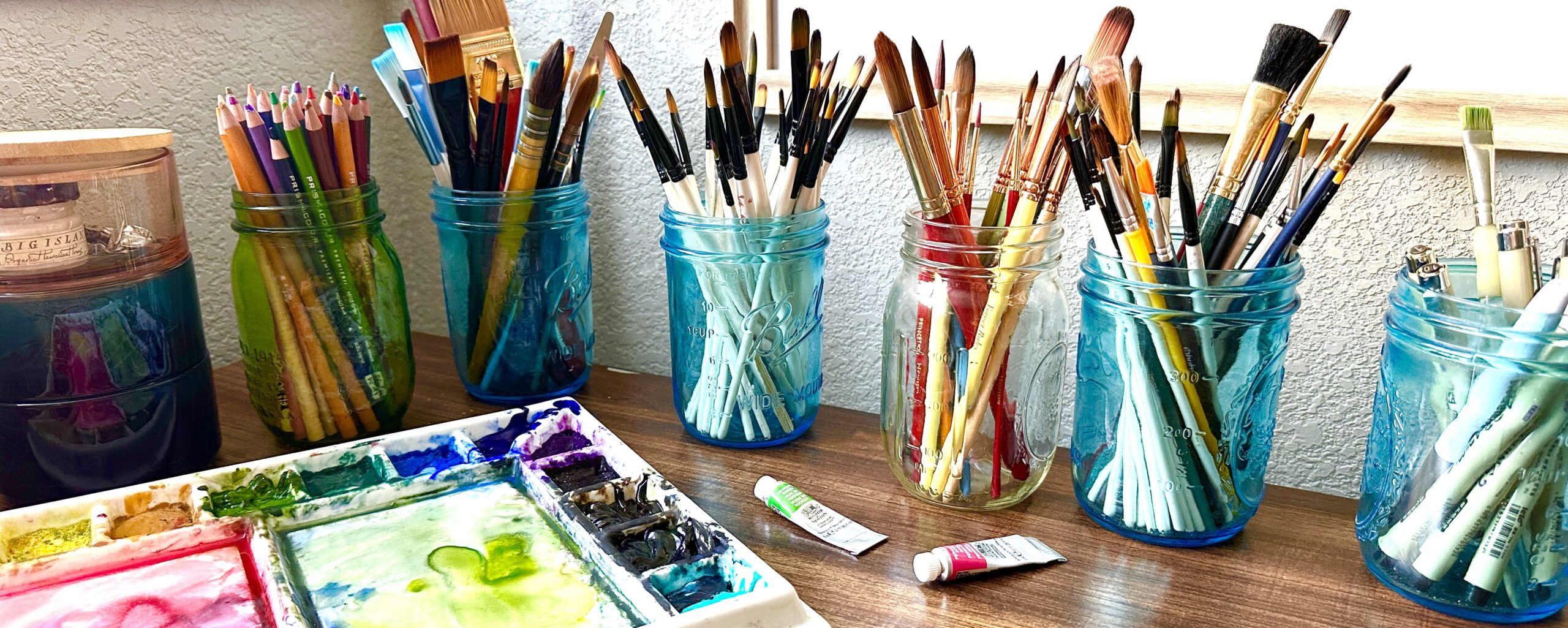 watercolor supplies with paint palette and paint brushes in glass jars