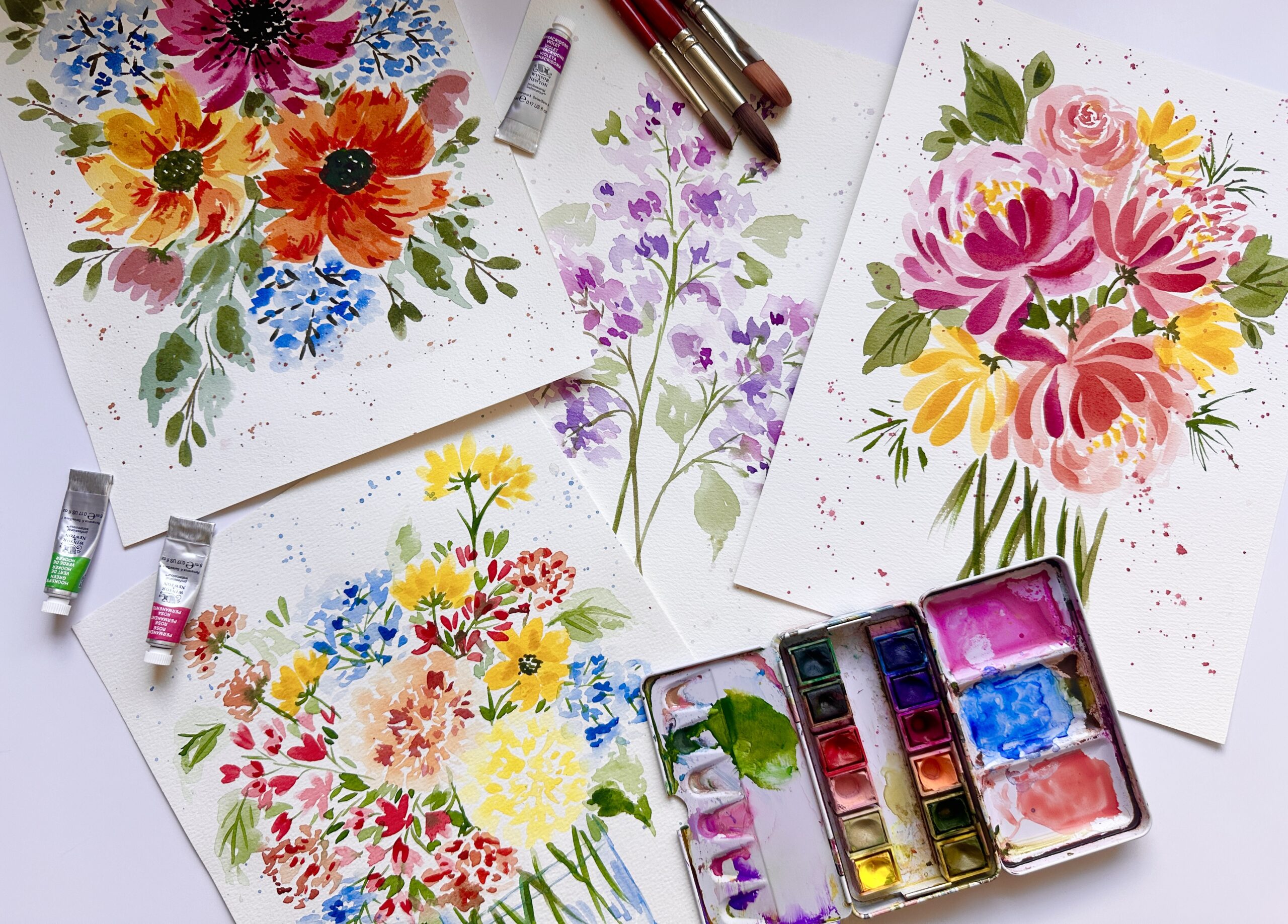 Watercolor flower paintings on a table with watercolor brushes and paints